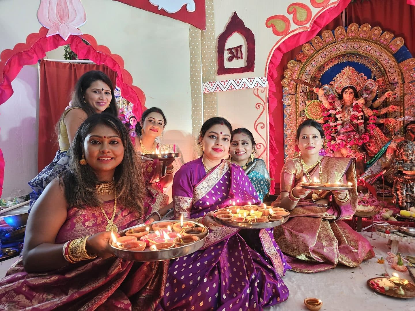 Women offering arati with diya plates in front of Maa Durga